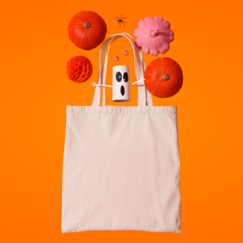 Canvas tote bag on bright orange background with pumpkins, pink pumpkin, ghost decoration and spider – Halloween tote bag banner.
