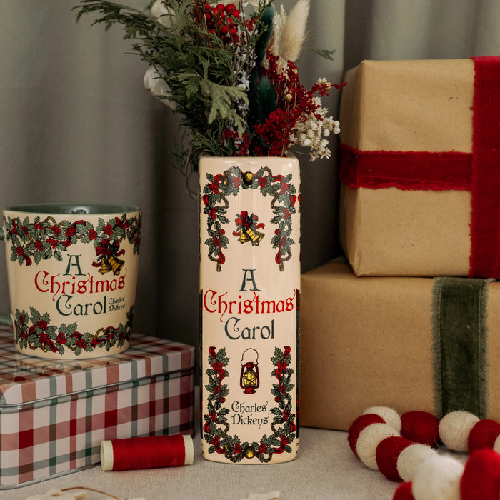 Ceramic A Christmas Carol book vase styled with festive stems beside matching mug and wrapped gifts