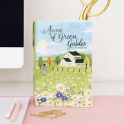 Book‑shaped vase on a workspace holding scissors beside notepad and paperclips

