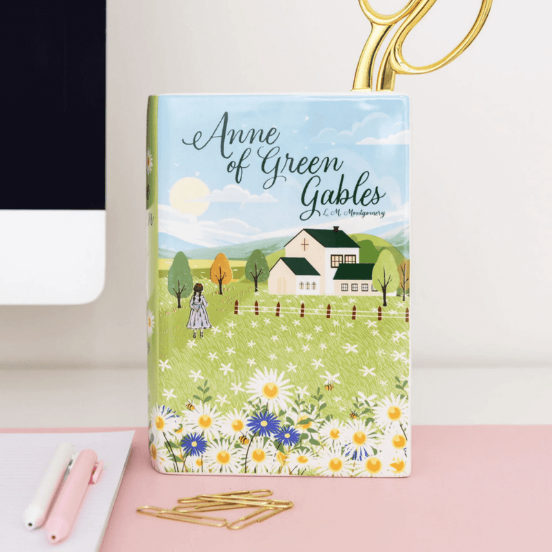 Book‑shaped vase on a workspace holding scissors beside notepad and paperclips

