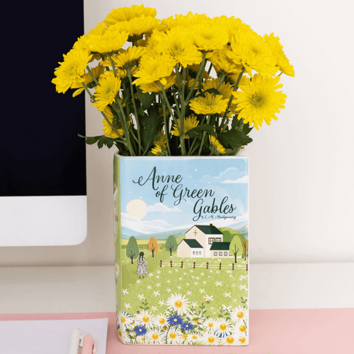 Anne of Green Gables ceramic book vase filled with bright yellow mums on a desk


