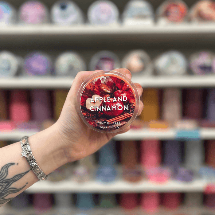 Apple and Cinnamon wax melt pot held in hand with colourful wax melt display in the background