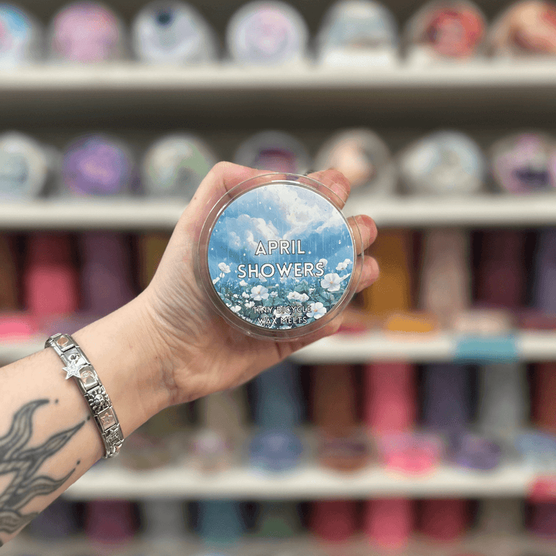 April Showers wax melt pot held in hand with colourful wax melt display in the background