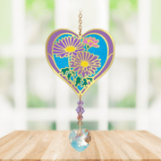 Close-up of heart-shaped Aster Crystal Suncatcher with purple aster motif and faceted rainbow-making heart drop hanging in a sunny window

