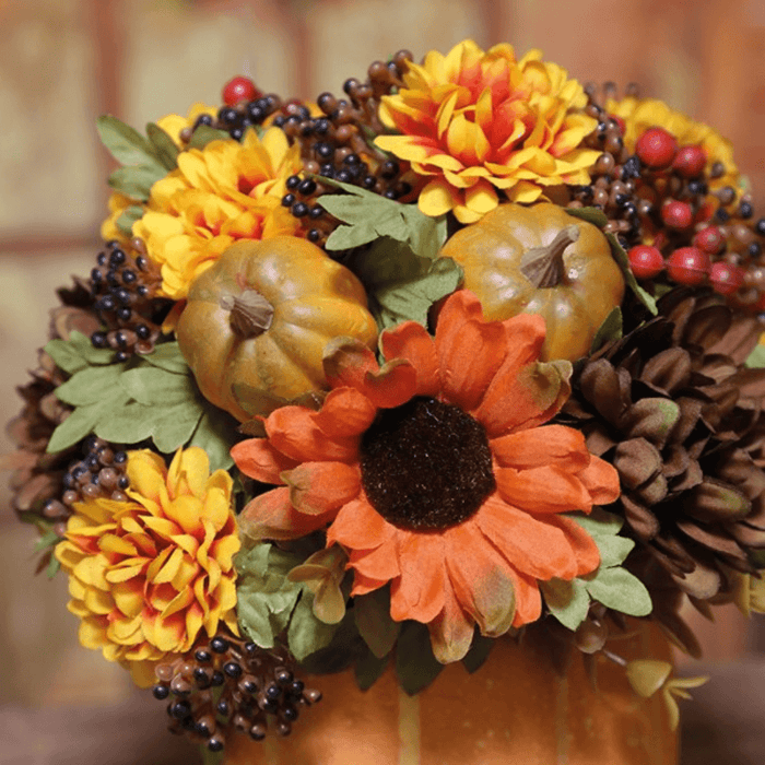 Close-up of orange daisy, golden flowers, berries and mini pumpkins in an orange ceramic vase for autumn home décor.