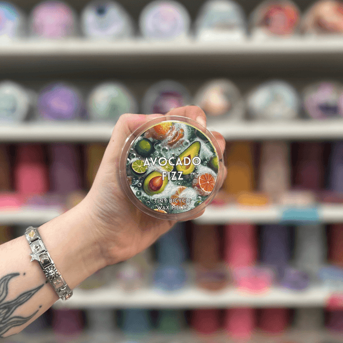 Avocado Fizz wax melt pot held in hand with colourful wax melt display in the background