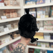 Mini Squishable Baby Mothman plush toy held in store, showing its black fluffy face, wings and cute spooky design
