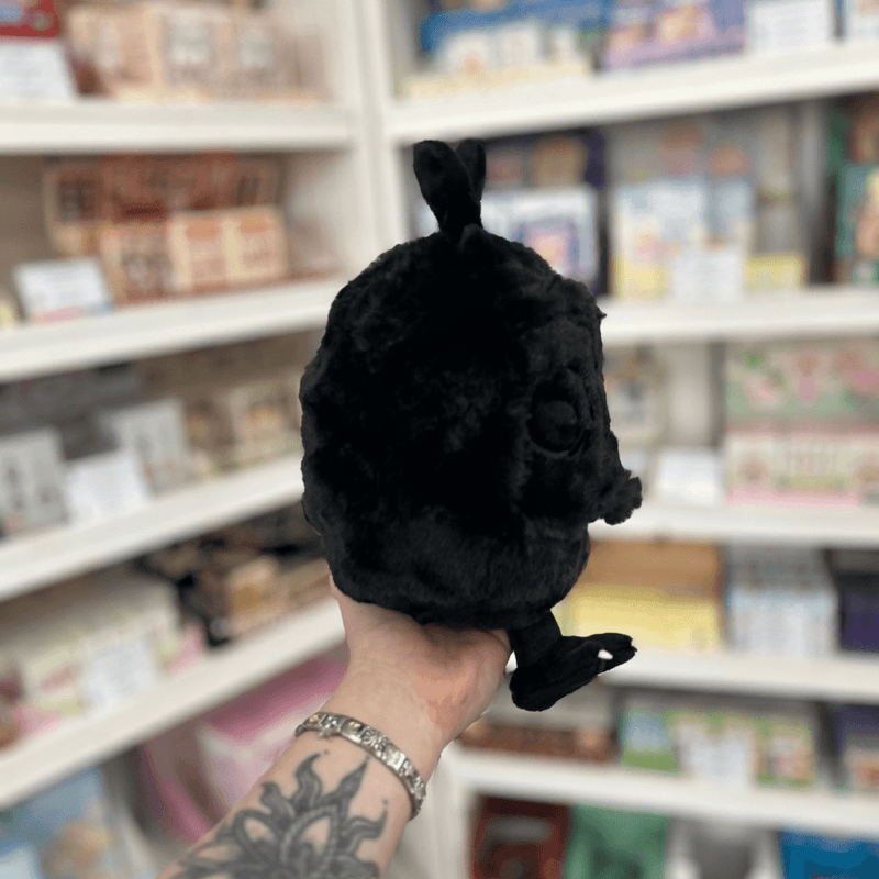 Mini Squishable Baby Mothman plush toy held in store, showing its black fluffy face, wings and cute spooky design