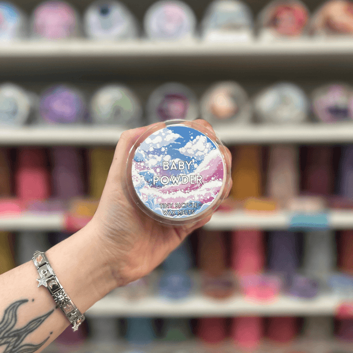Baby Powder wax melt pot held in hand with colourful wax melt display in the background
