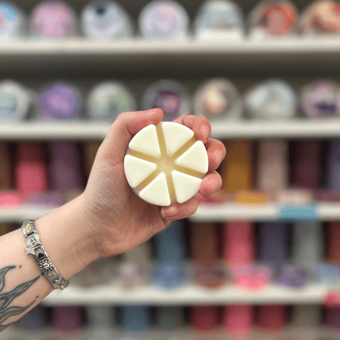 Baby Powder wax melt segments held in hand with colourful wax melt display in the background