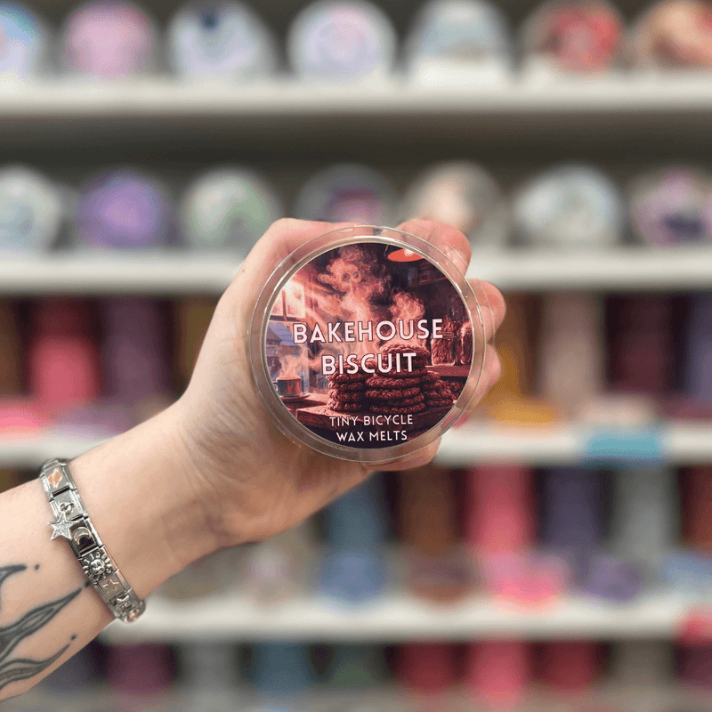 Bakehouse Biscuit wax melt pot held in hand with colourful wax melt display in the background