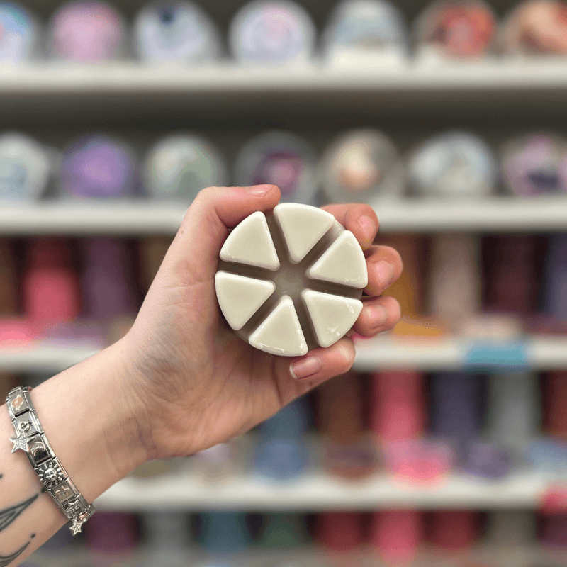 Bakehouse Biscuit wax melt segments held in hand with colourful wax melt display in the background