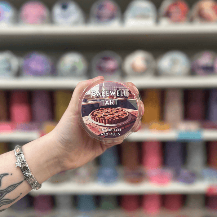 Bakewell Tart wax melt pot held in hand in front of a colourful wax melt display