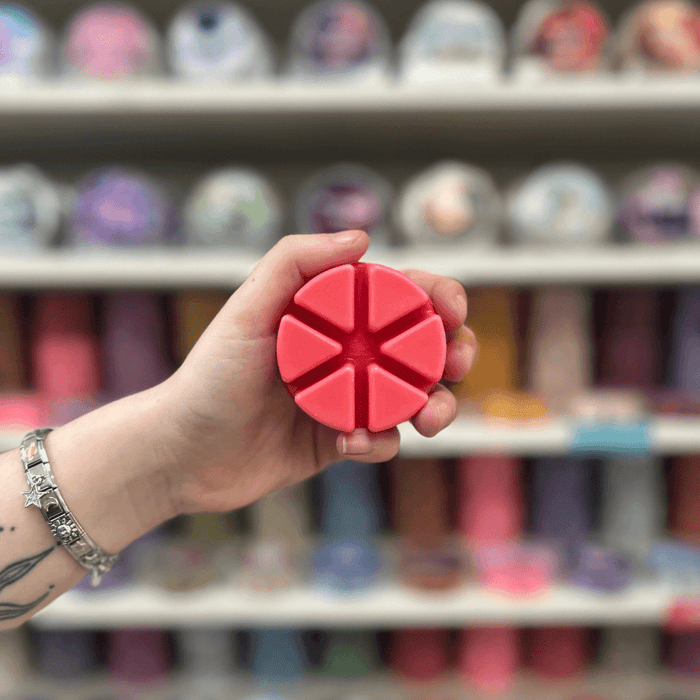 Bright pink segmented wax melt held in hand with colourful wax melts blurred in the background