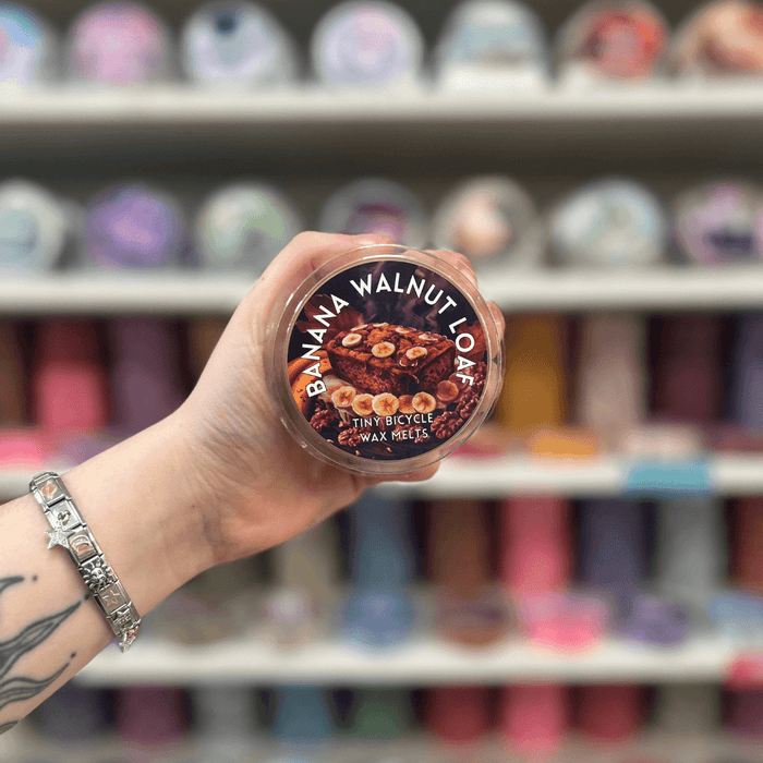 Banana Walnut Loaf wax melt pot held in hand with colourful wax melt display in the background
