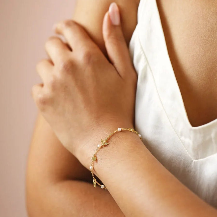 Model wearing a delicate gold charm bracelet with pearls and tiny bee, butterfly, heart and star charms.