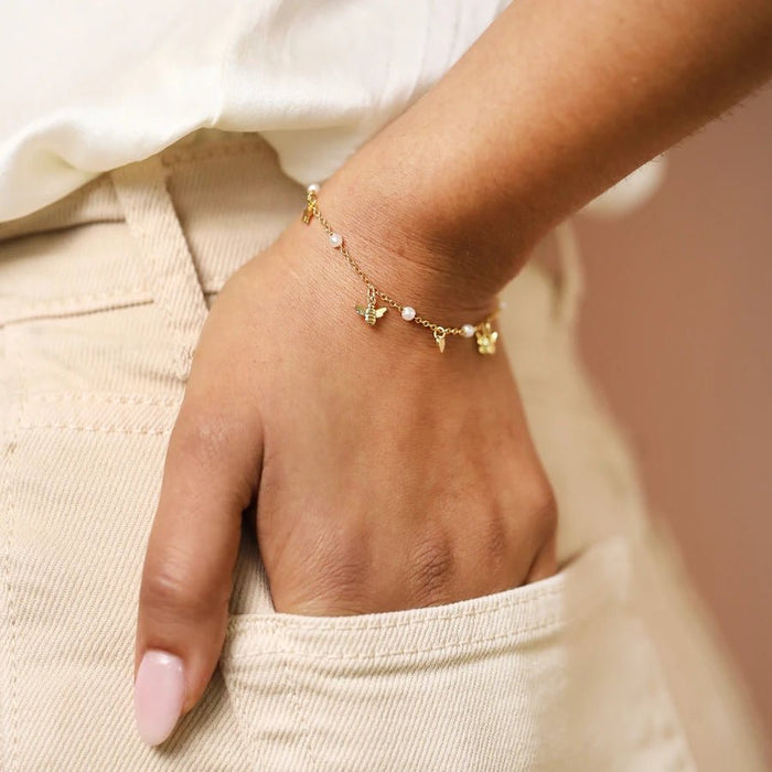 Dainty gold bracelet with small pearls and bee, heart and butterfly charms worn on the wrist for a delicate everyday look.