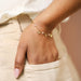 Dainty gold bracelet with small pearls and bee, heart and butterfly charms worn on the wrist for a delicate everyday look.