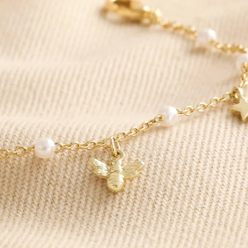 Macro detail of the gold bee charm and mini pearls on a delicate gold-tone bracelet.