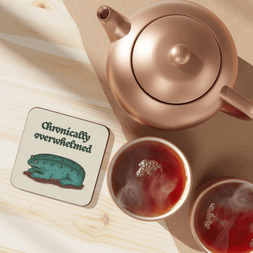 Betiobca Chronically Overwhelmed frog coaster shown on a table beside tea cups and a teapot