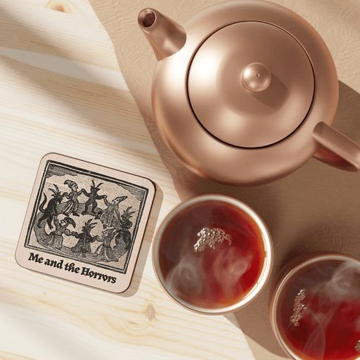 Betiobca Me and the Horrors gothic coaster shown on a table beside tea cups and a teapot