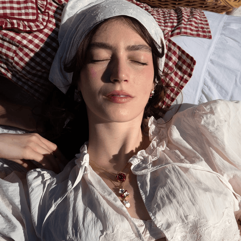 Model wearing Bill Skinner Strawberry and Hanging Mouse Pendant with a second strawberry necklace and white ruffled blouse