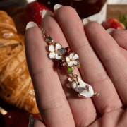 Hand holding Bill Skinner's gold-plated Strawberry and Hanging Mouse pendant showing glossy enamel berries, flowers and white mouse