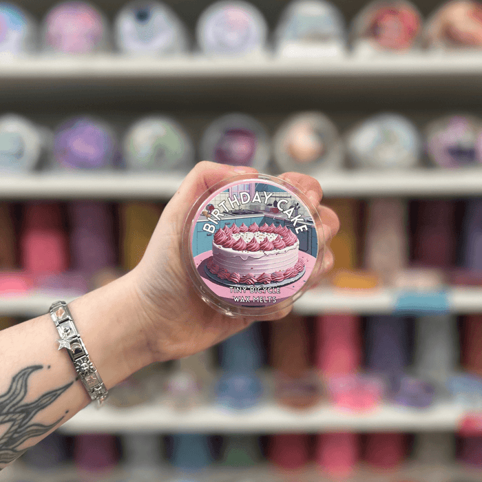 Birthday Cake wax melt pot held in hand with colourful wax melt display in the background