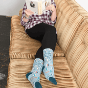 Model lounging on sofa wearing Blue Q Fuck Off I’m Reading women’s crew socks in blue with book pattern