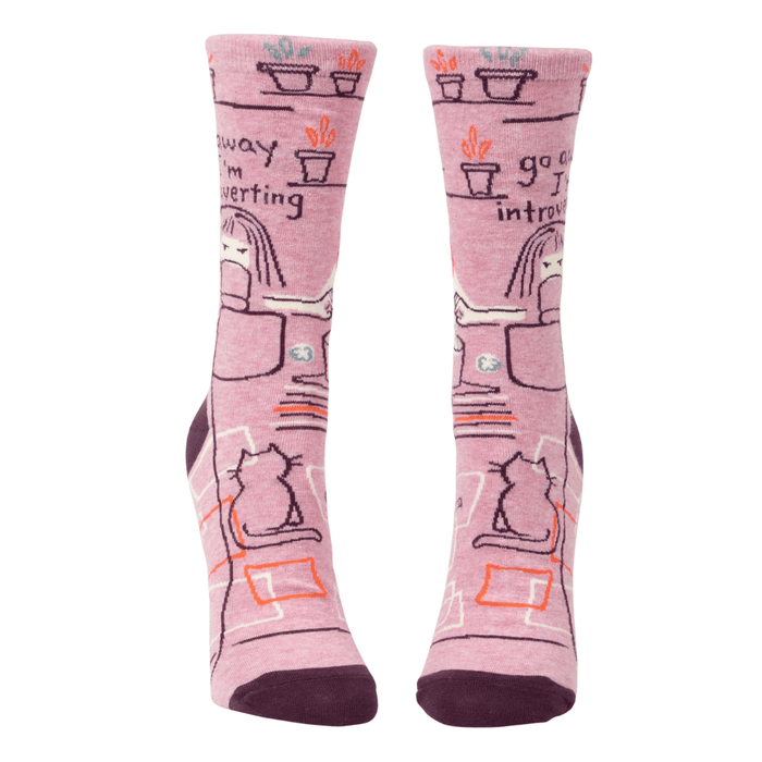 Front view of Blue Q women’s crew socks in pink with plum cuffs and toes, desk-and-cat illustration and the slogan go away I’m introverting