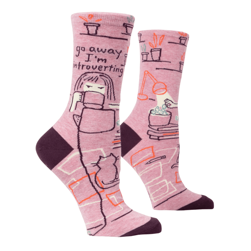 Angled view of Blue Q pink crew socks showing go away I’m introverting slogan with plants, desk and cat graphic, plum heel and toe