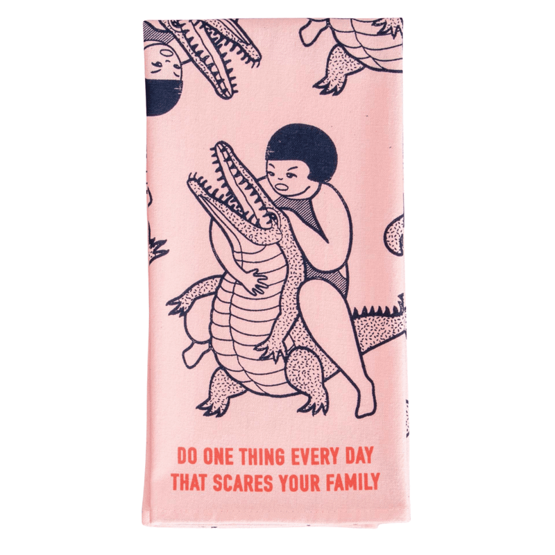 Front of Blue Q Do One Thing That Scares Your Family tea towel with crocodile-wrestling design