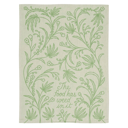 Blue Q tea towel laid flat with leafy pattern and text The food has weed in it