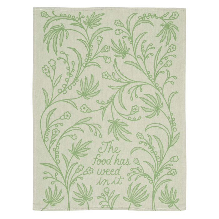 Blue Q tea towel laid flat with leafy pattern and text The food has weed in it