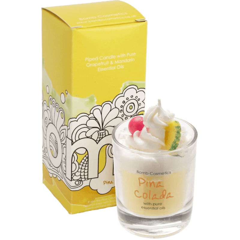 Bomb Cosmetics Piña Colada piped scented candle topped with wax fruit garnish, shown beside its sunny yellow gift box.