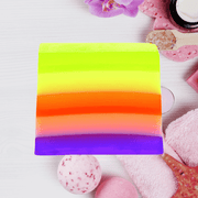 Bomb Cosmetics Pure Therapy Soap Slice with rainbow layers styled in a spa flatlay with towels and bath items