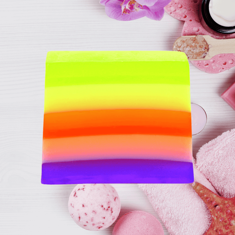 Bomb Cosmetics Pure Therapy Soap Slice with rainbow layers styled in a spa flatlay with towels and bath items