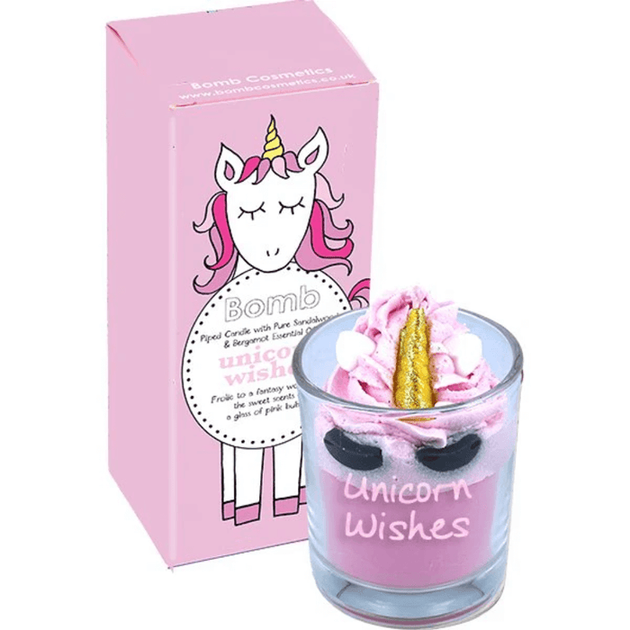 Bomb Cosmetics Unicorn Wishes piped scented candle—pink whipped wax with gold horn topper, beside matching pastel unicorn gift box.