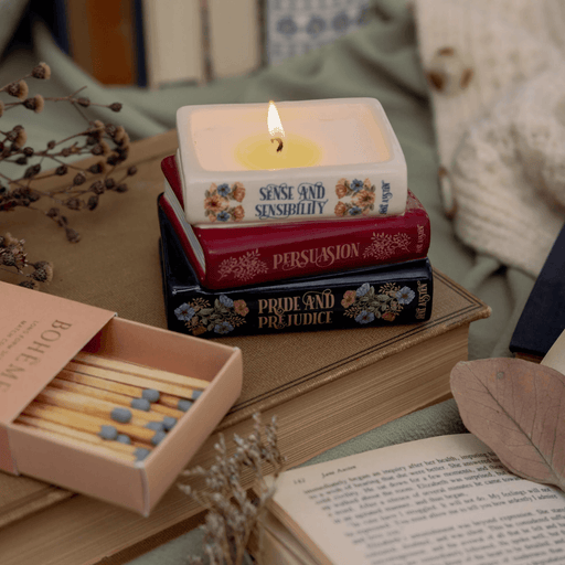 Jane Austen book stack shaped candle lit on a book with matches and dried flowers
