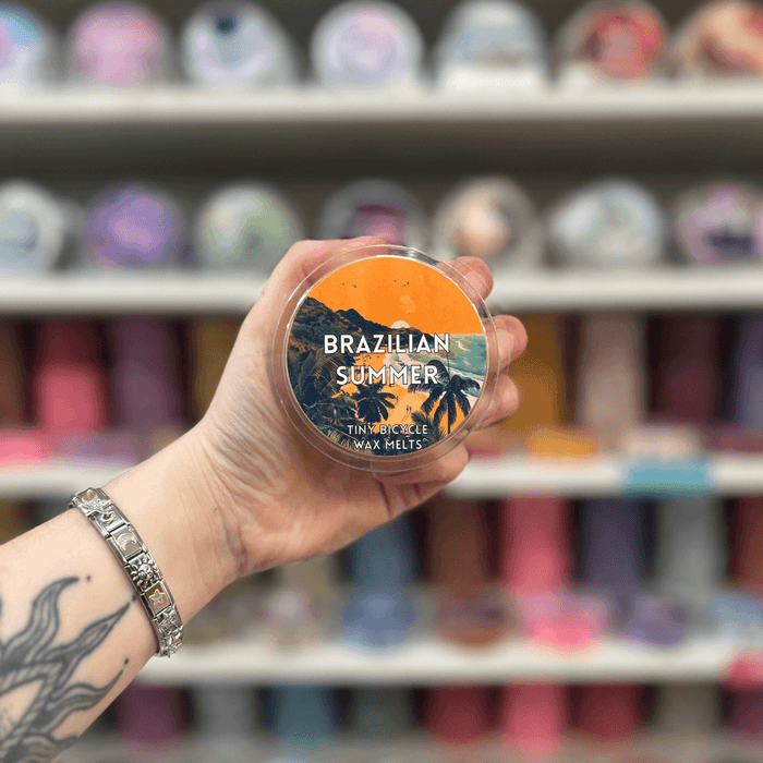 Brazilian Summer wax melt pot held in hand with colourful wax melt display in the background