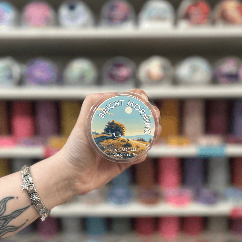 Bright Morning wax melt pot held in hand with a colourful wax melt shelf in the background