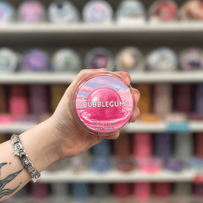 Bubblegum wax melt pot held in hand with colourful wax melt display in the background