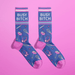 Pair of blue women’s novelty crew socks with pink accents and Busy Bitch text, sprinkled with cocktail glasses, headphones, whisks and stars.