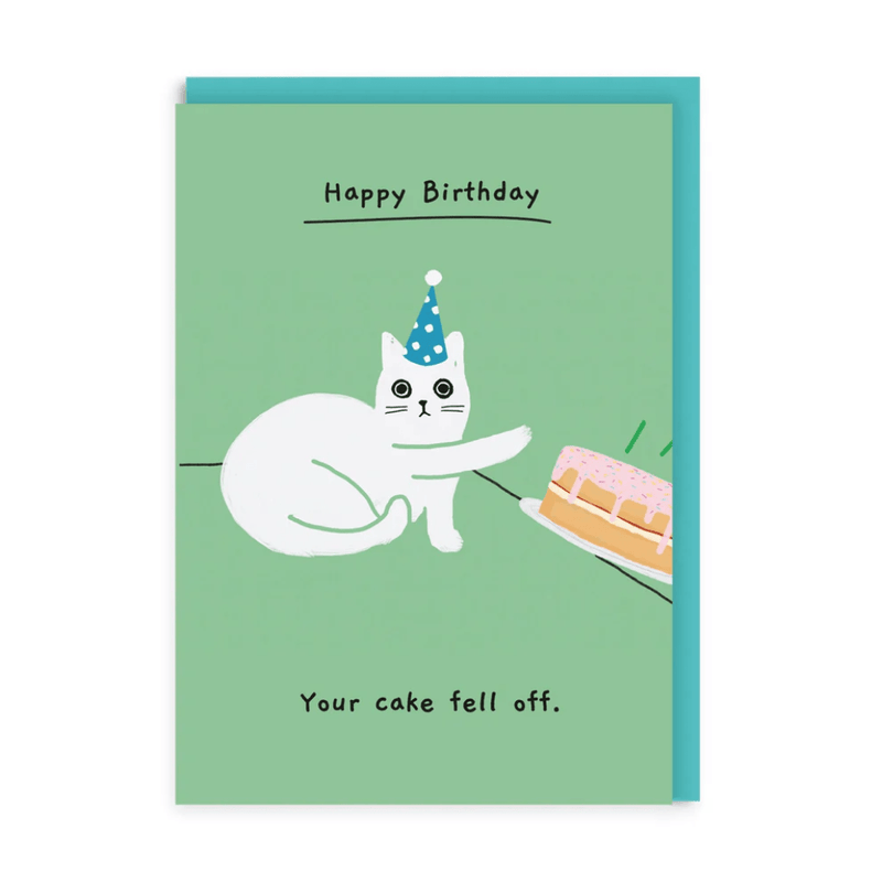 Funny birthday greeting card – white cat in blue party hat knocking cake off table
