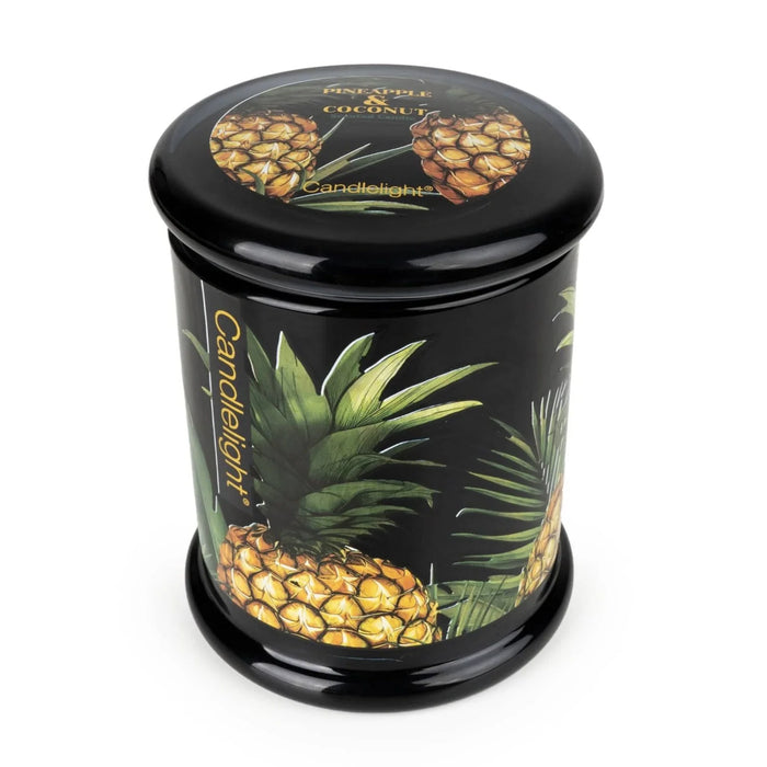 Angled view of Candlelight Pineapple & Coconut large glass lidded jar candle with black lid and tropical pineapple design.