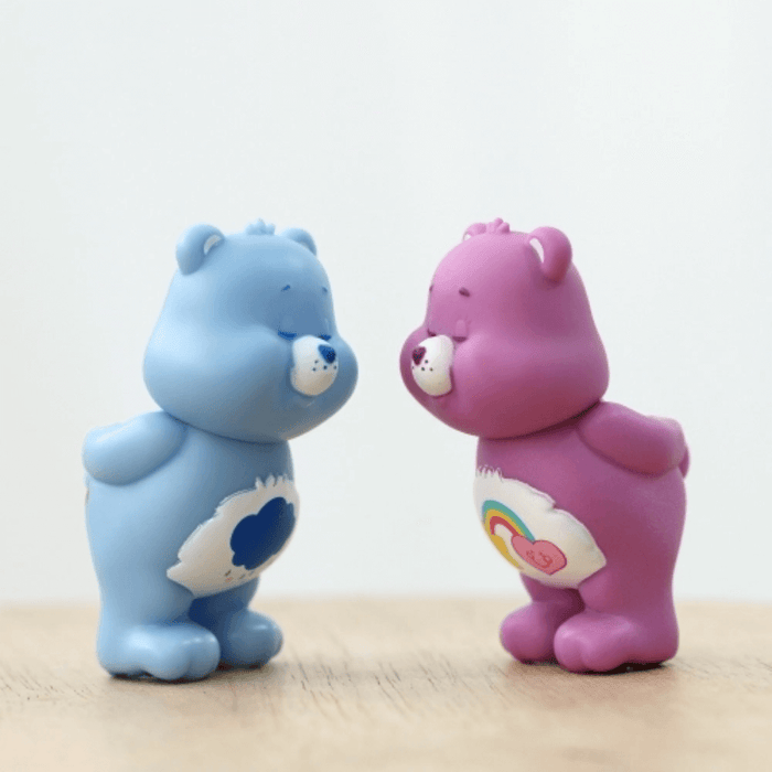 Blue Grumpy Bear and purple Best Friend Bear mini figures facing each other on a wooden surface