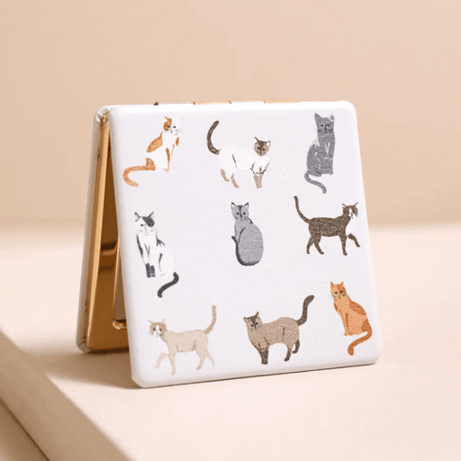 Closed square compact mirror with grey and ginger cat print on a white PU cover and gold-tone edges.