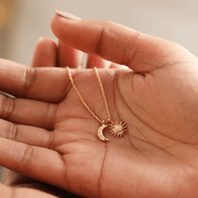 Gold sun and moon charm necklace held in a hand to show pendant size, with cubic zirconia crystal details.