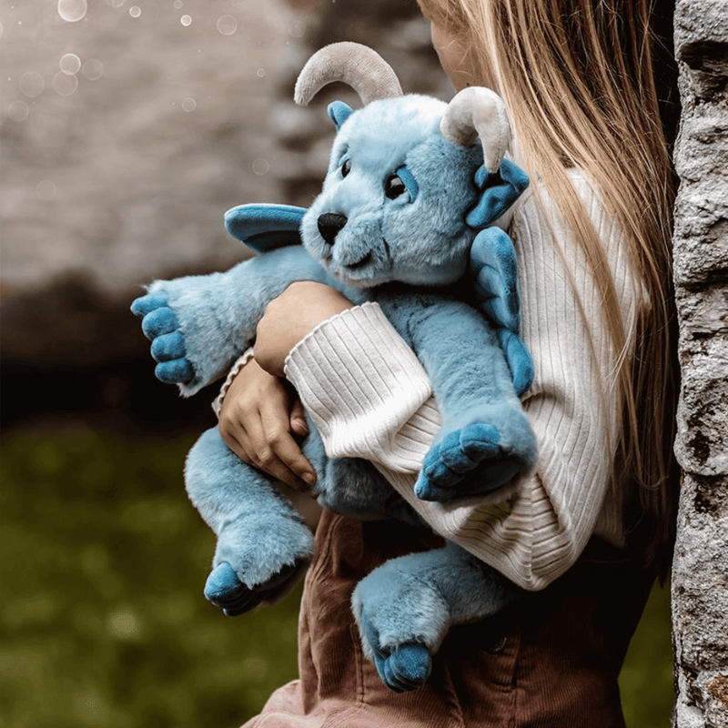 Child cuddling Drawbridge, a sky-blue Bearhouse by Charlie Bears plush gargoyle with soft wings and curled horns