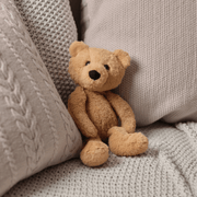 Charlie Bear oatmeal-brown plush teddy sitting between cushions on a sofa